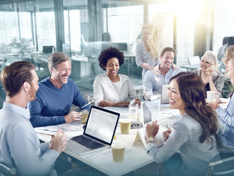 A diverse group of professionals laughing and collaborating around a conference table in a bright modern office, symbolizing strong workplace culture, employee engagement, and teamwork.